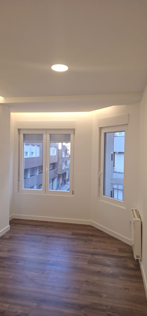 Salón de piso reformado integralmente en León con foseado de luz indirecta en el techo y suelo laminado de madera