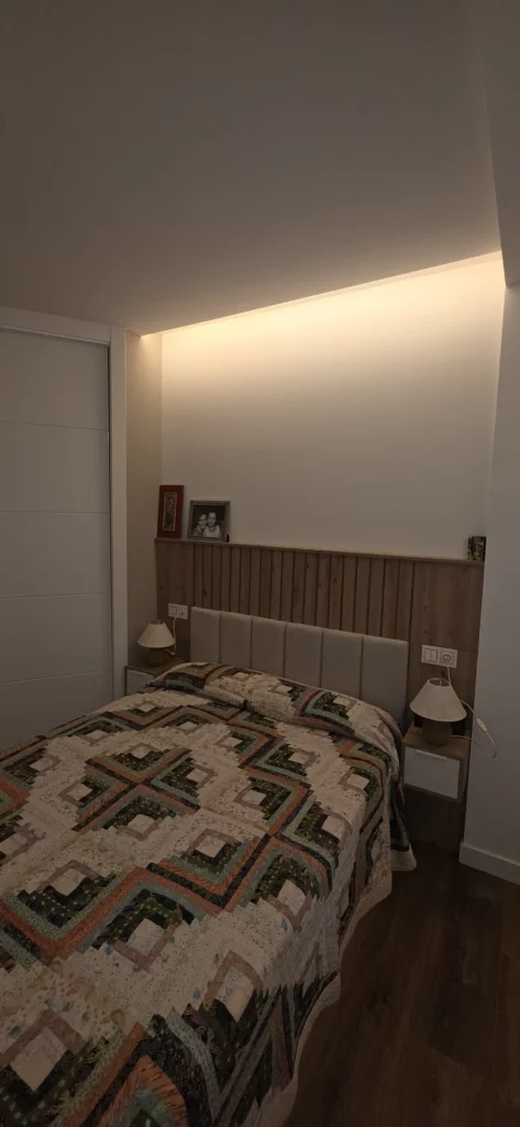 Dormitorio con cabecero de madera a medida e iluminación LED indirecta en reforma integral en León