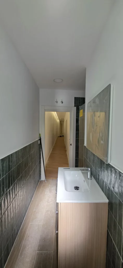 Baño reformado con azulejo verde a media altura, mueble de madera y bañera en piso de León