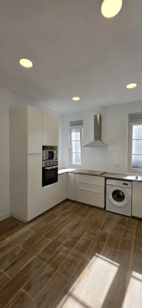 Cocina blanca en L con campana de acero y suelo efecto madera tras reforma integral de piso en León