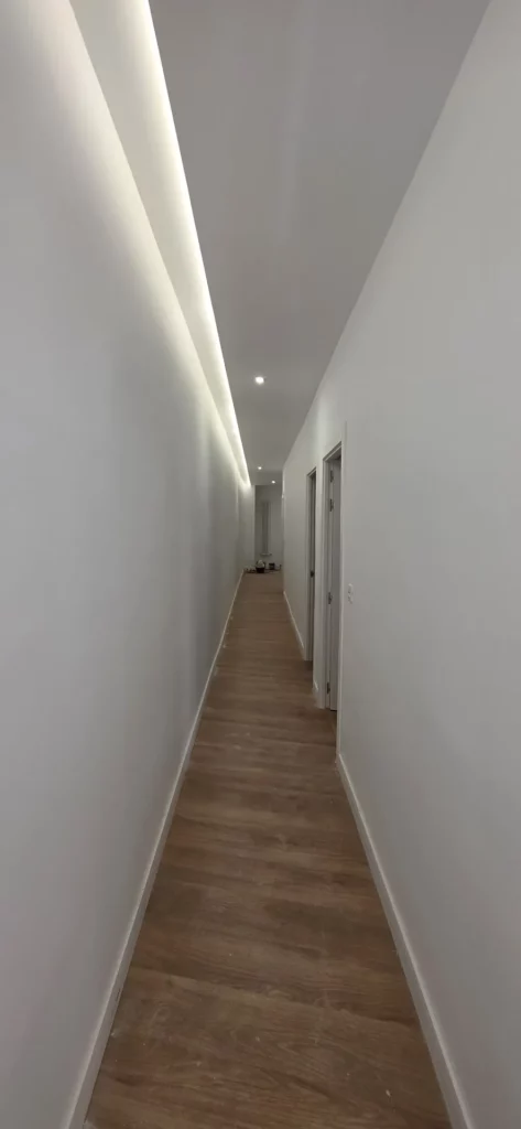 Pasillo de piso reformado en León con foseado de luz LED indirecta y suelo efecto madera